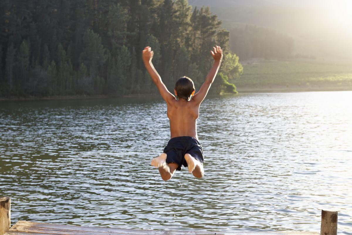 A boy jumping off a dock into Mokowanis Lake.