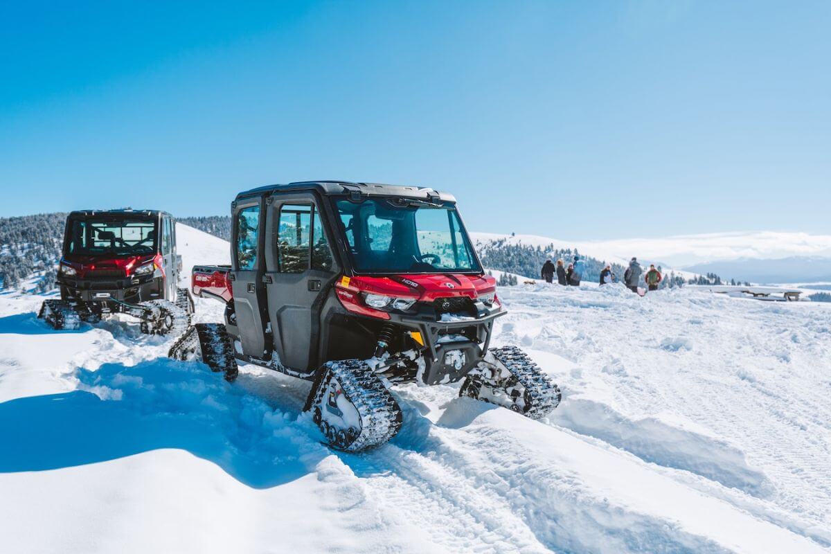 Two tracked UTVs navigate through snowy terrain as a group of adventurers enjoy the wintry surroundings during a UTV tour with The Ranch at Rock Creek in Montana.