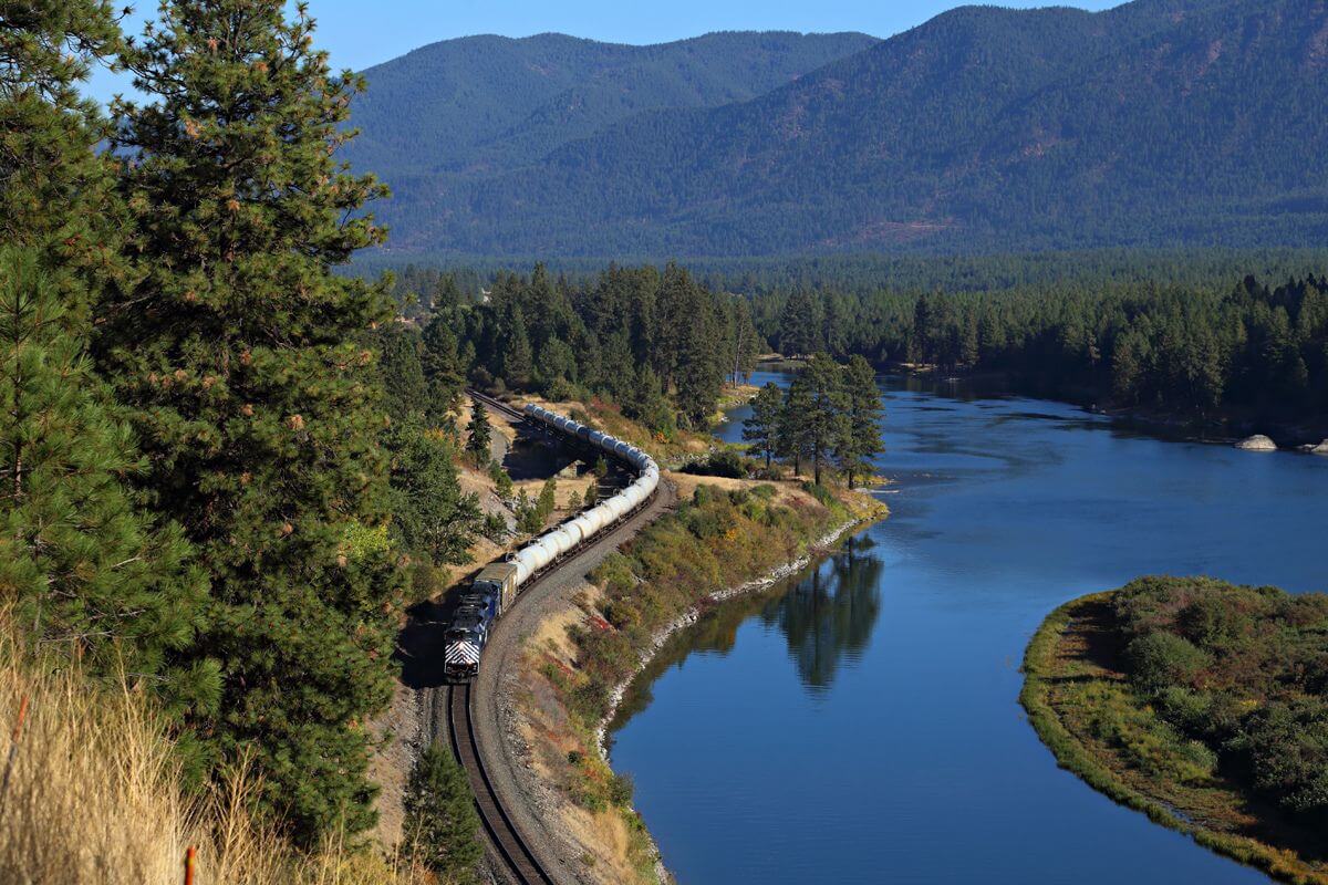 A train travels along a track by the river in Montana