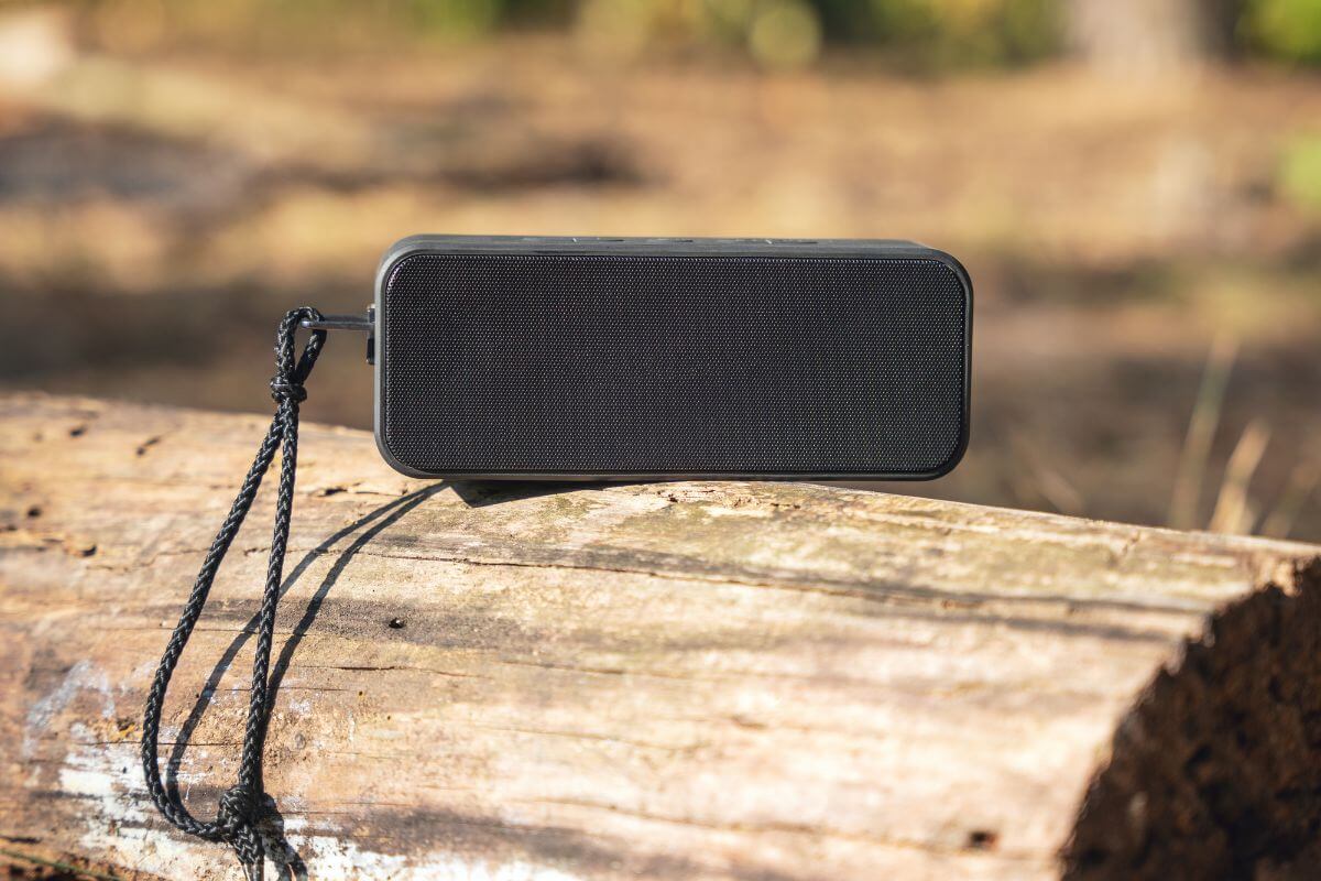 A portable black speaker rests on a wooden log, playing recorded animal sounds, which is prohibited according to Montana hunting regulations.