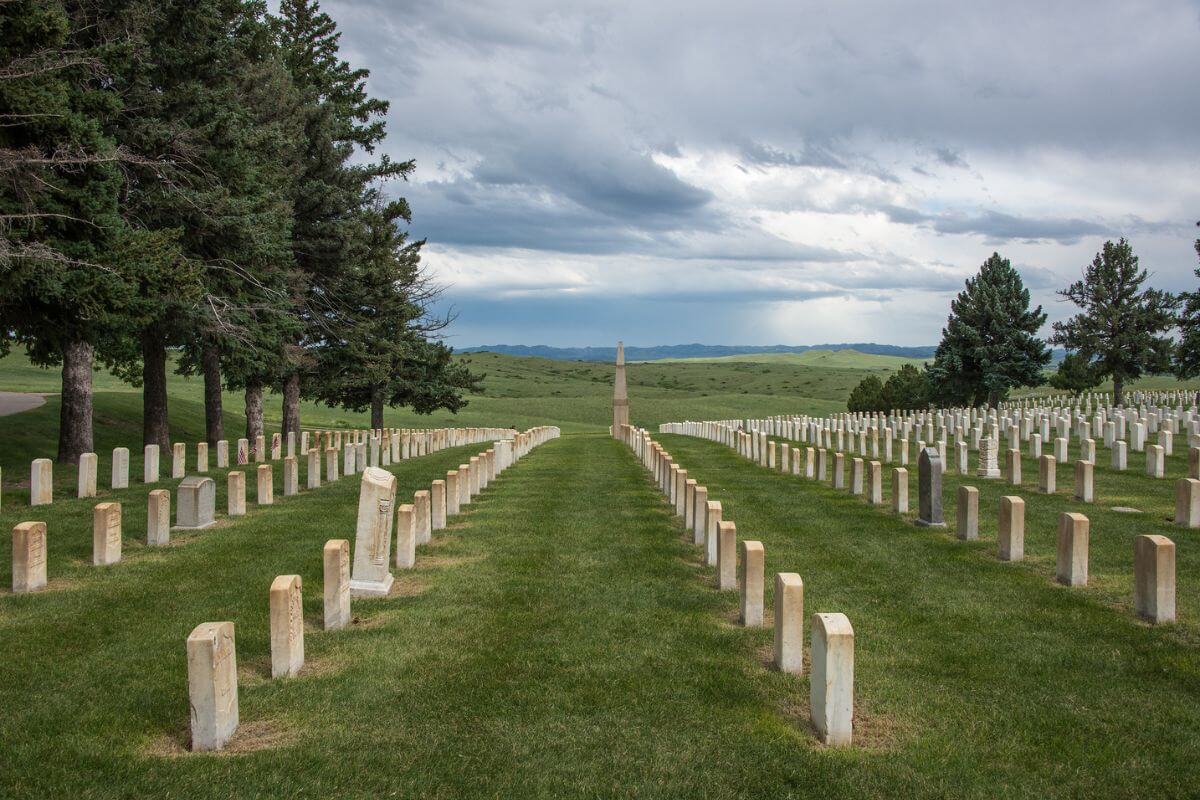 A row of graves in a grassy field under a cloudy sky at the Little Bighorn Battlefield National Monument.