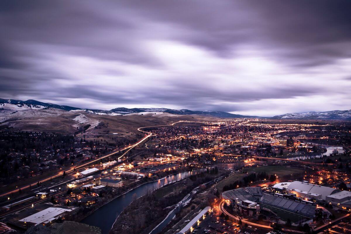 An aerial view of a Montana city at night with mountains in the background.