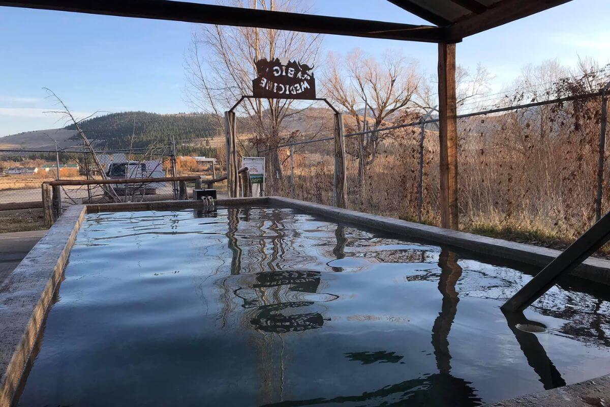A view of Big Medicine Hot Springs' pool, featuring the welcome sign with mountains in the distance.