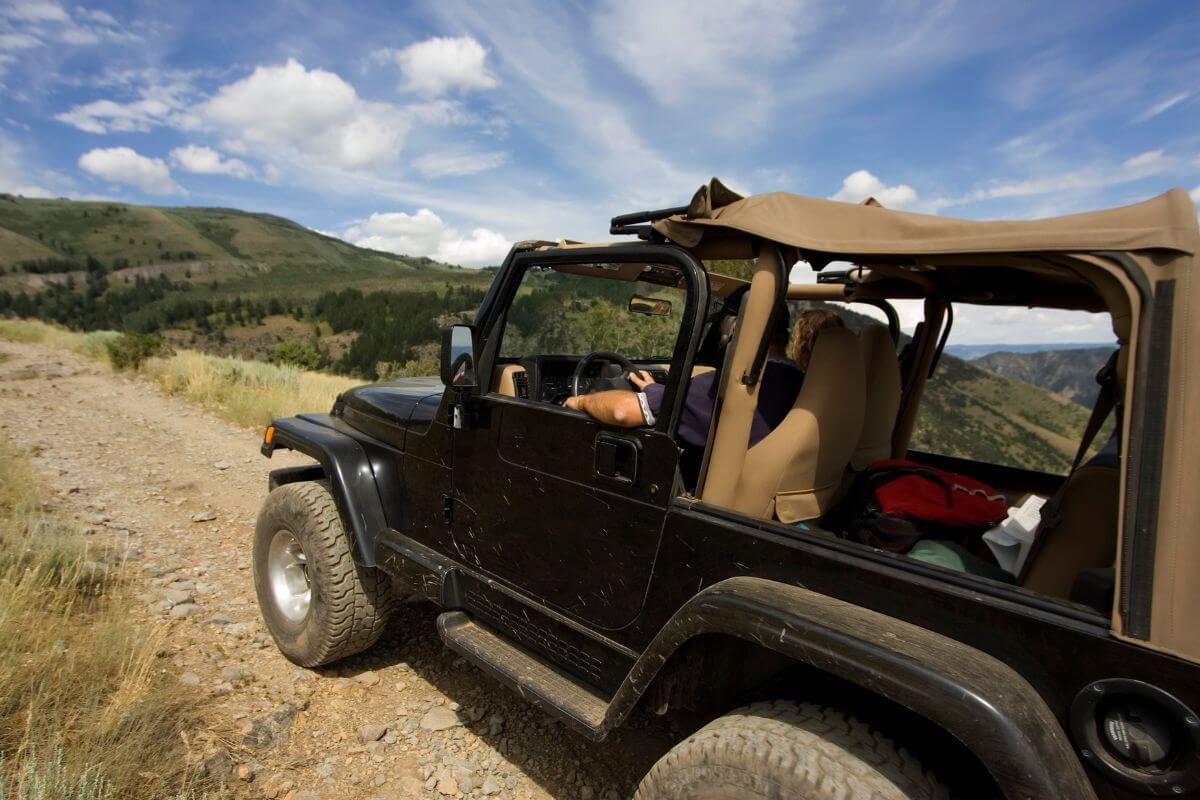 An open-top jeep drives along a dusty mountain trail during a jeep tour with Blackfeet Tours.