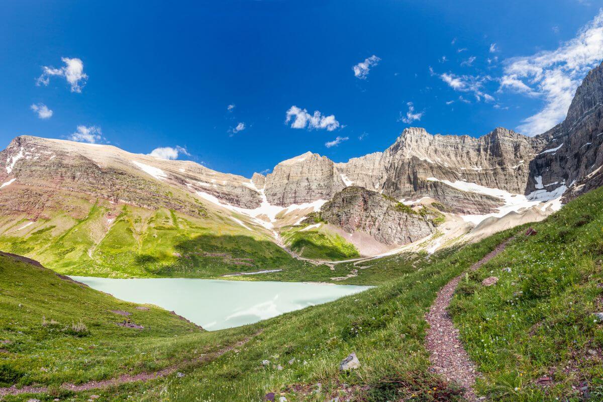 Cracker Lake Trail that features a tranquil lake with turquoise waters nestled between grassy fields and rugged, snow-dotted cliffs