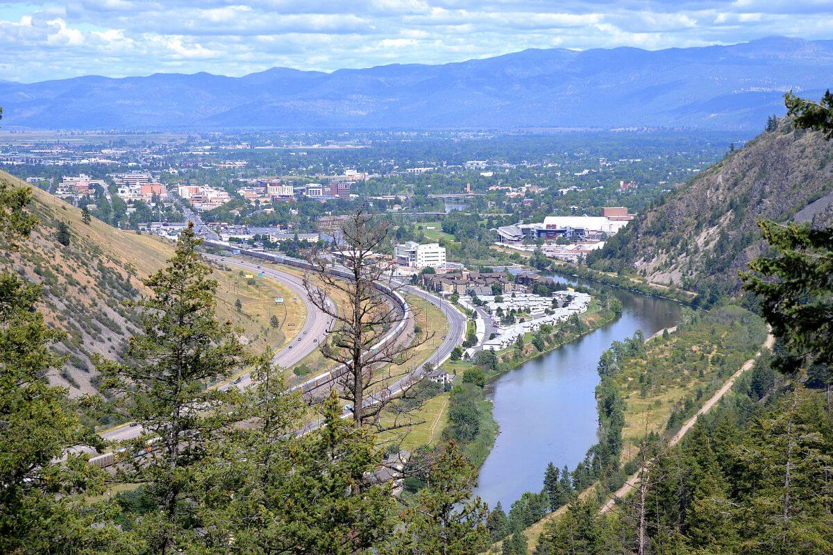 A view from the top of a mountain offering stunning vistas of a river and a bustling cityscape in Missoula, Montana.