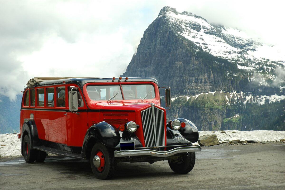 One of the classic Montana red bus tours from Glacier National Park Lodges parked on a mountain road.
