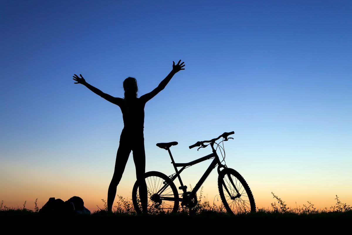 Silhouette of a Woman with her Hands Up Beside a Bicycle in Montana
