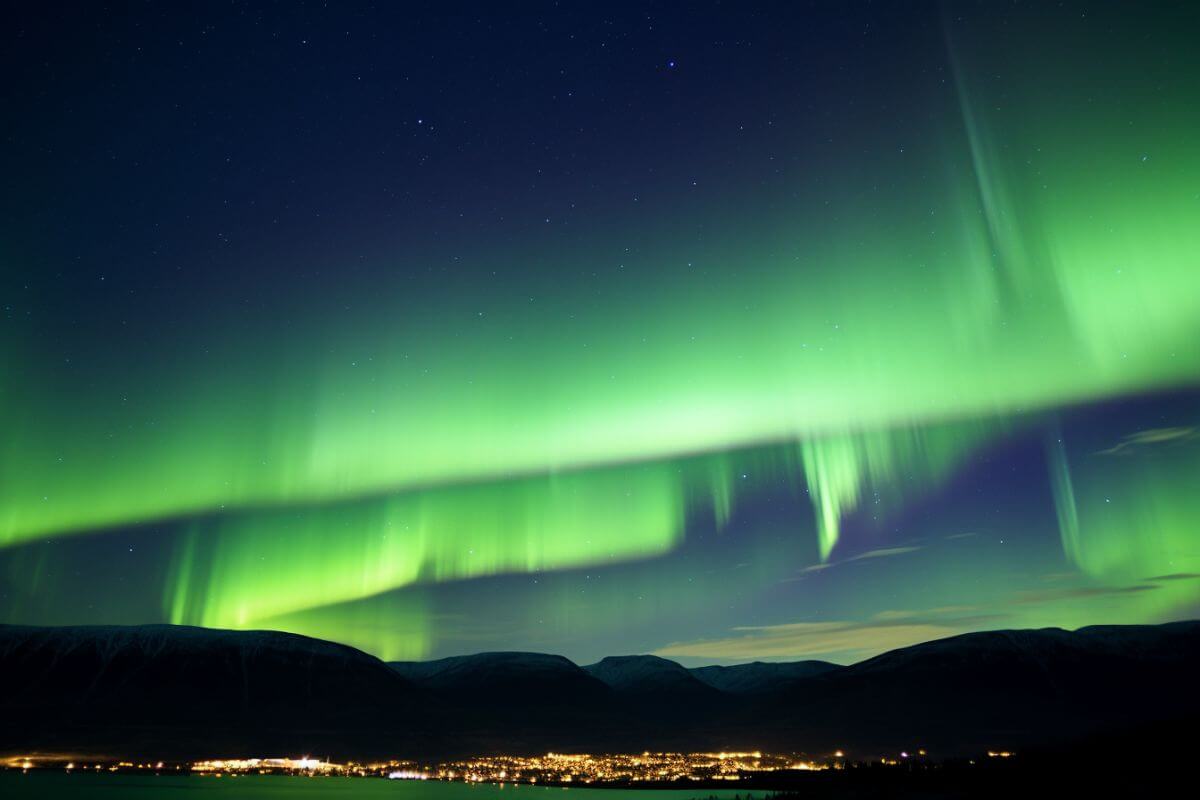 A stunning aurora borealis gracefully graces a picturesque Montana city nestled amid majestic mountains.