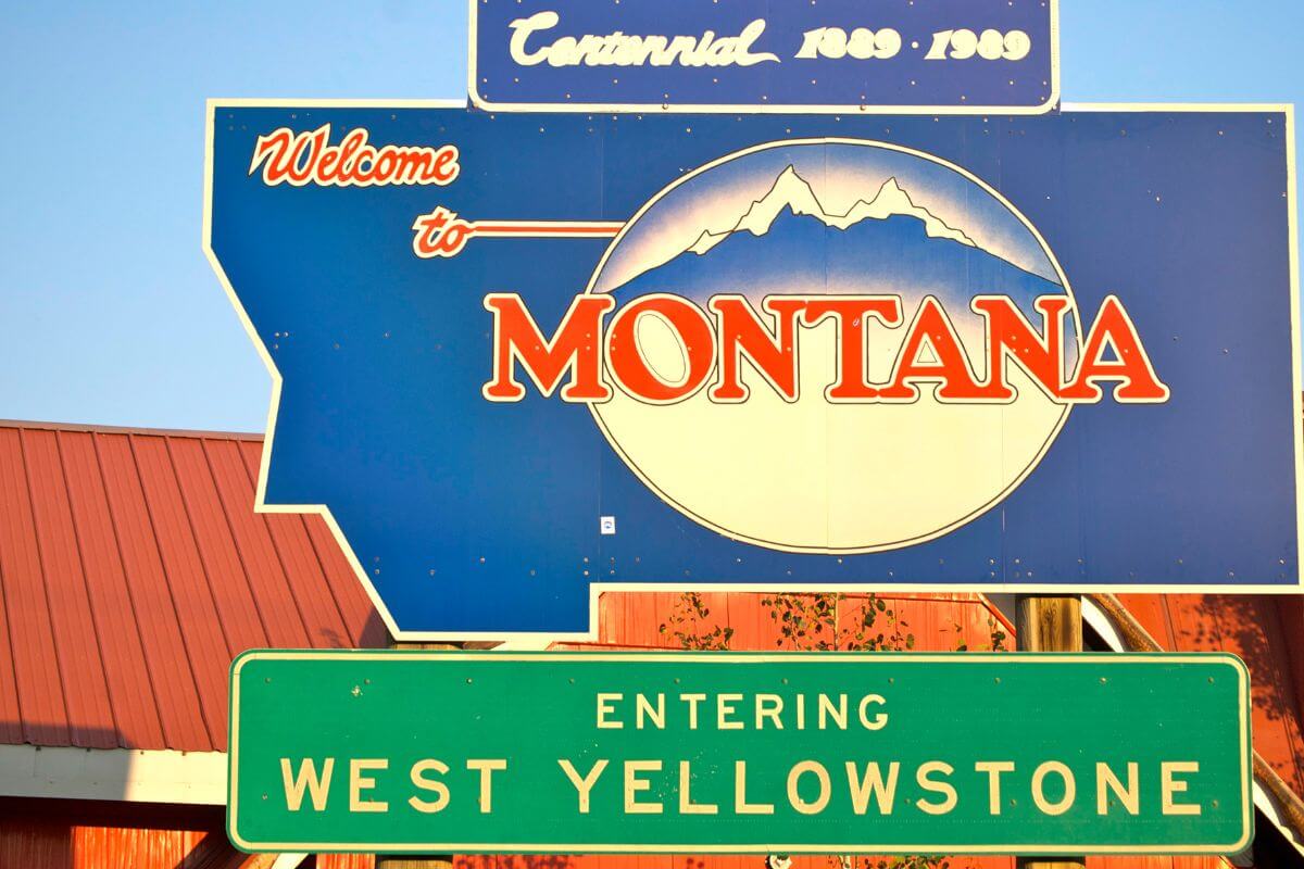 A 'Welcome to Montana' sign positioned above an 'Entering West Yellowstone' sign in Montana