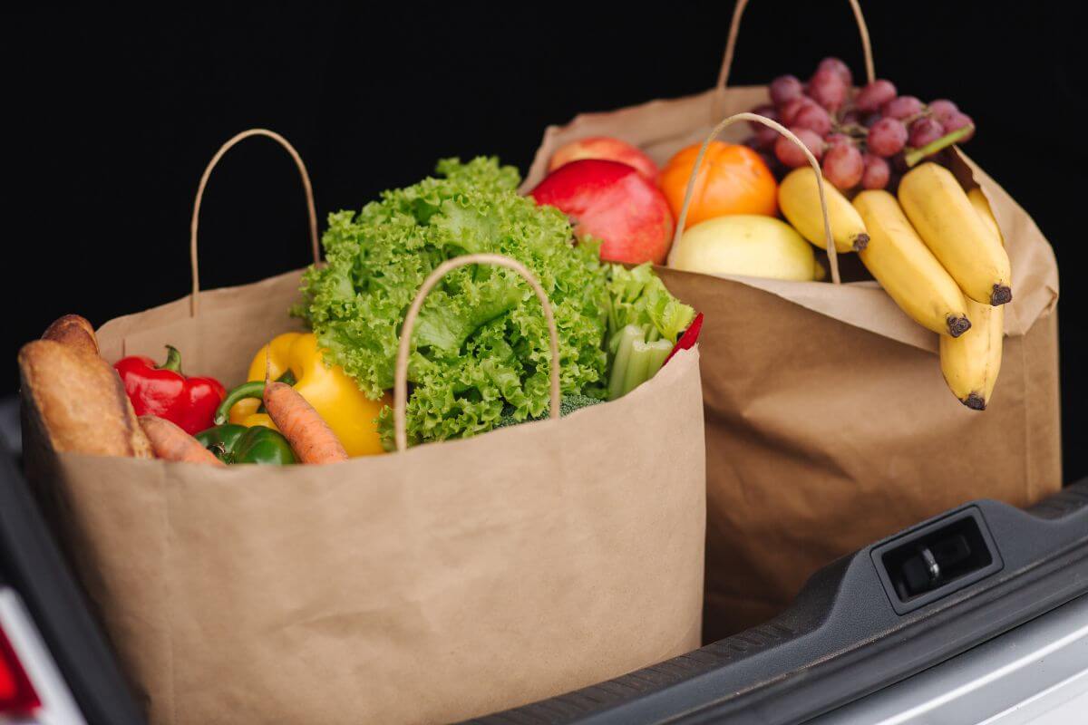 Two paper bags filled with fruits and vegetables in the trunk of a car