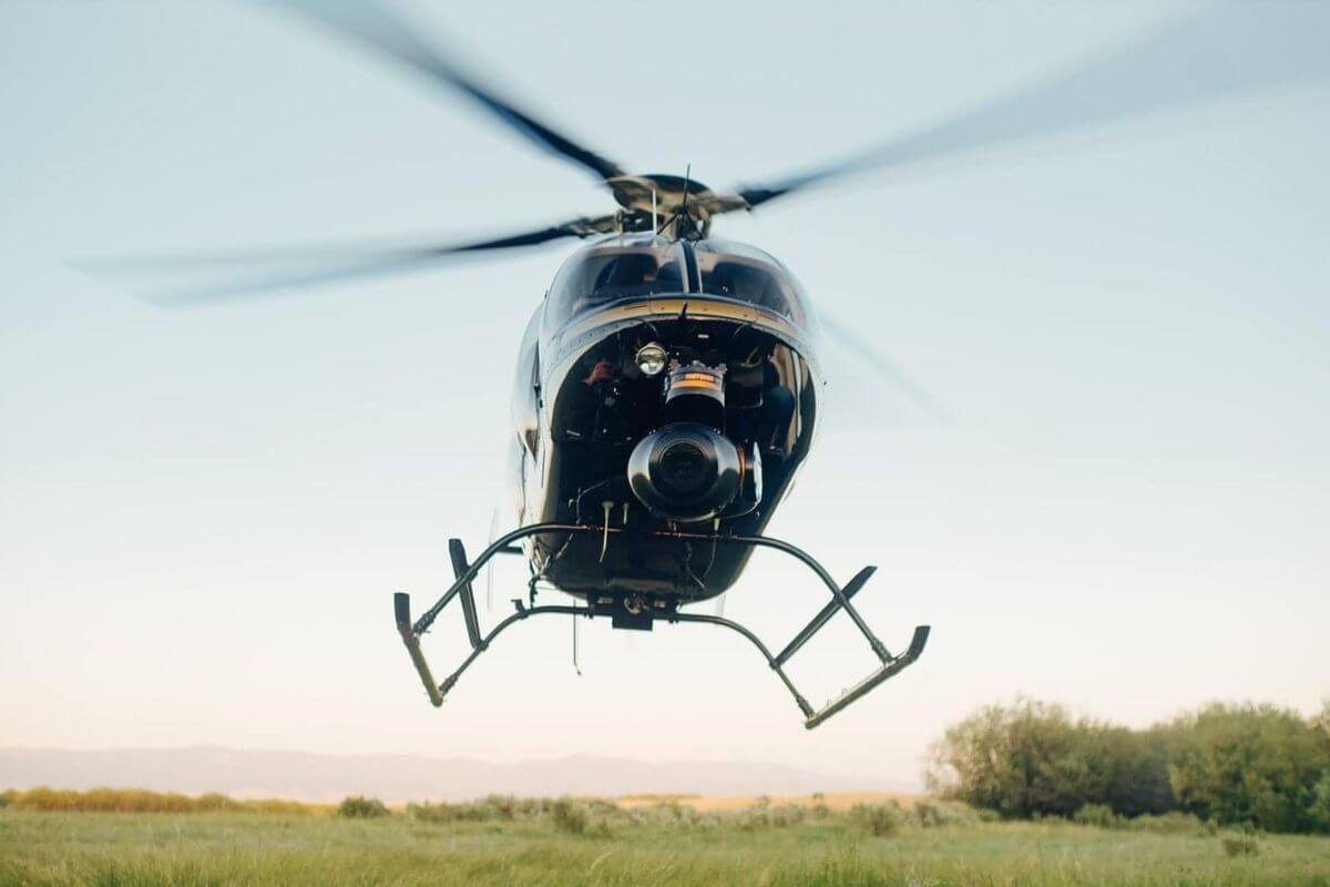 A Rocky Mountain Rotors helicopter in mid-flight against open fields and a clear sky during one of their Montana helicopter tours.