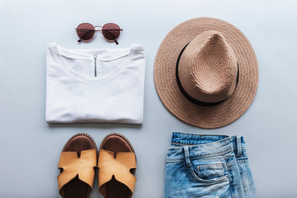 Clothing essentials, including a straw hat and jeans, are laid out on a blue background.