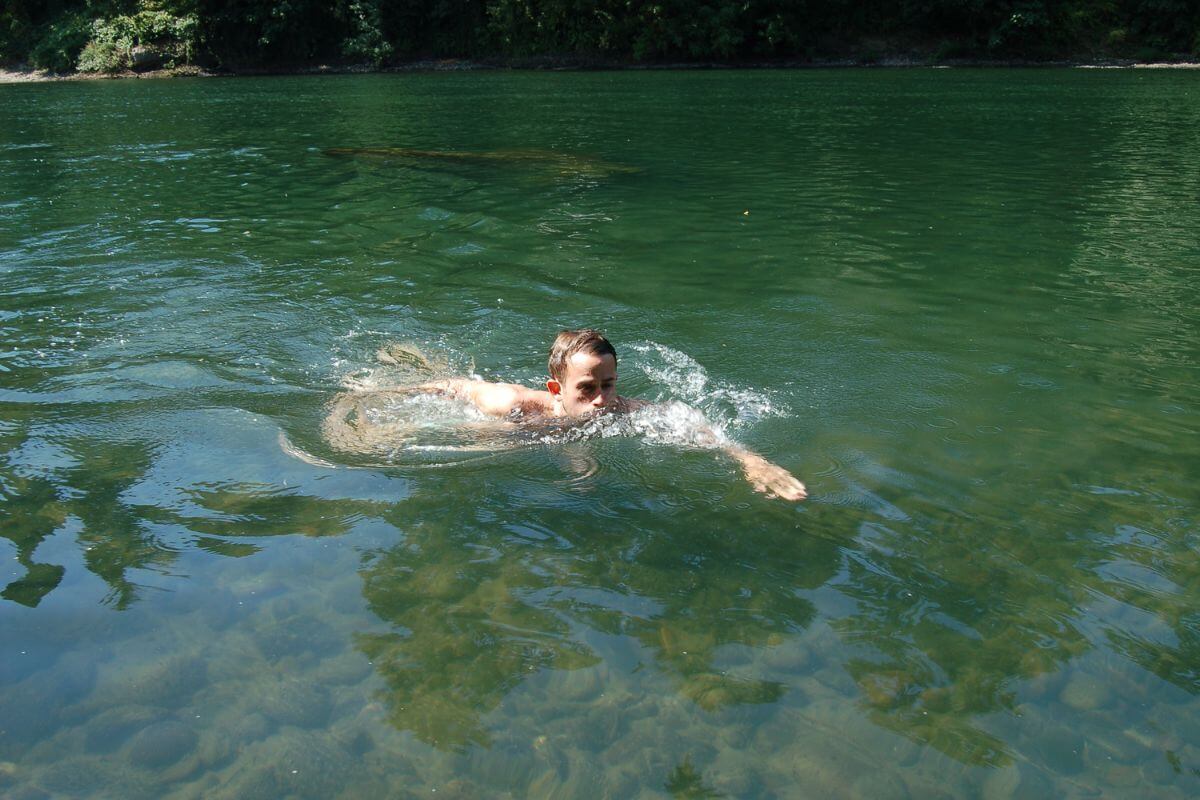 A person swims in the serene, clear green waters near the Little North Fork waterfall in Montana.
