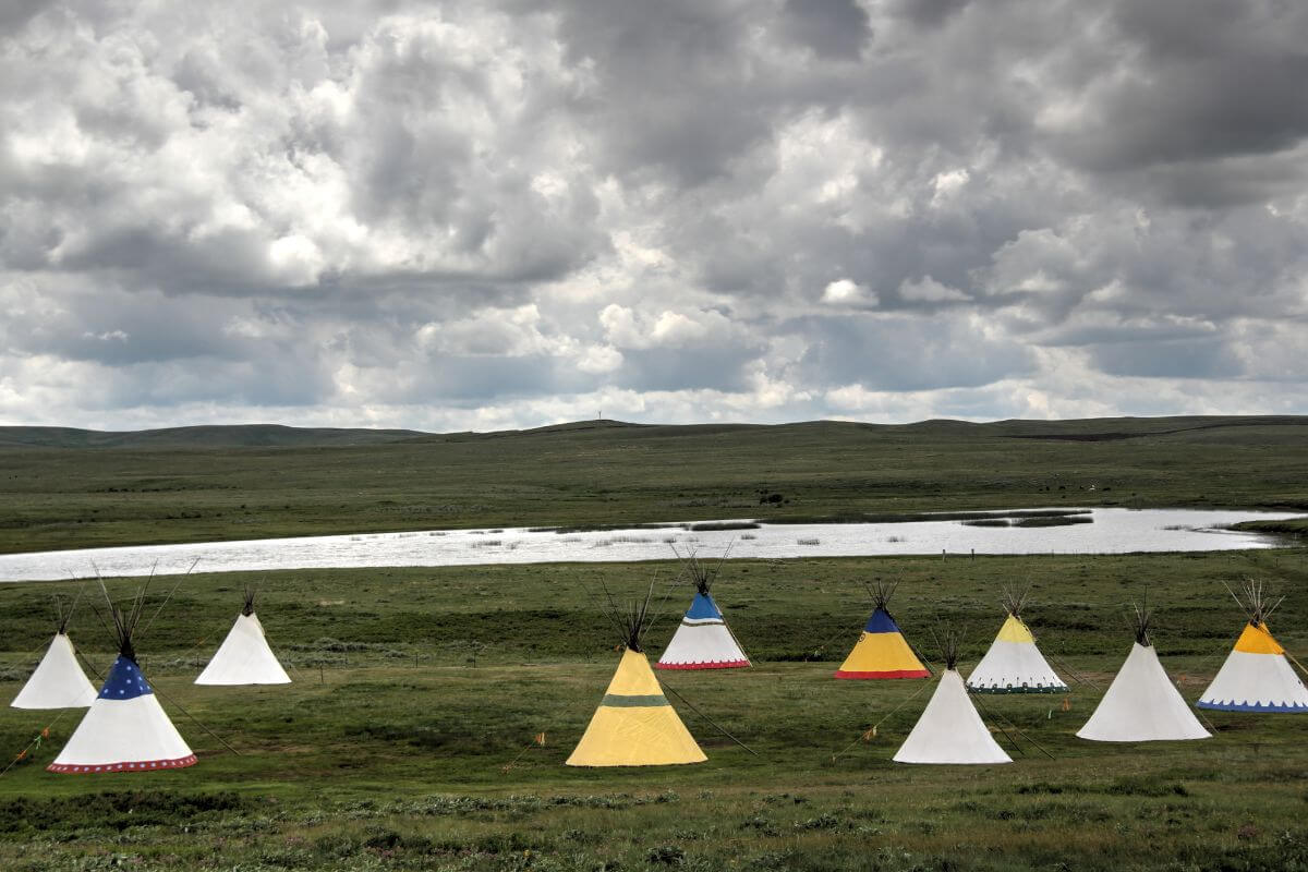 A group of teepees in a field under a cloudy sky in Montana.