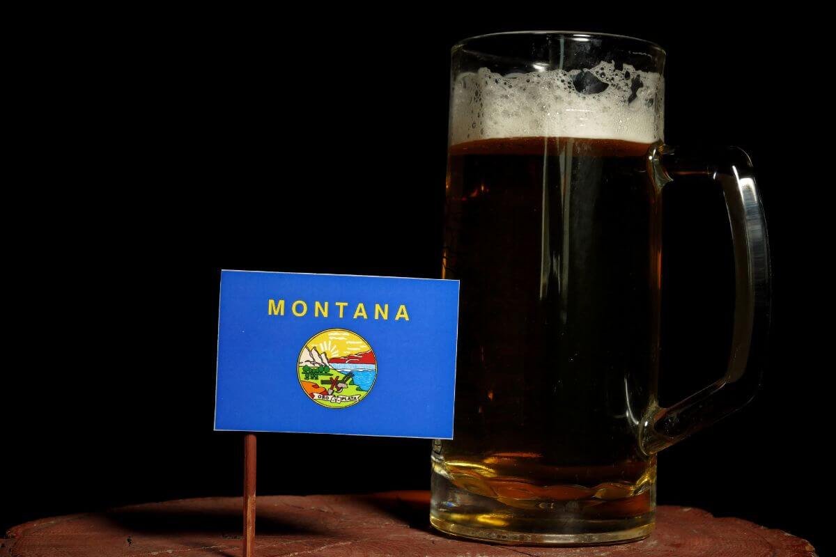 A Mug of Beer Next to a Miniature Version of the Montana Flag