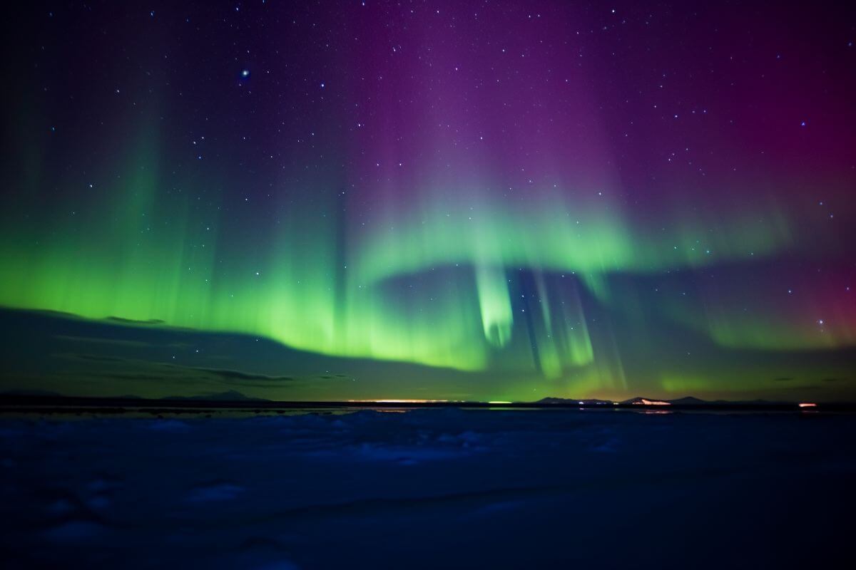 Green and purple polar lights shimmer over the Montana landscape.