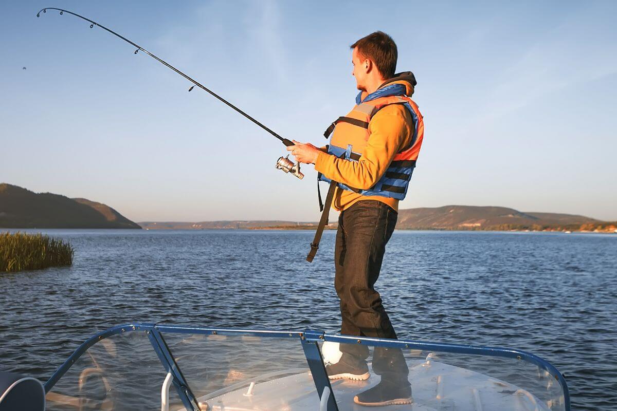 A man wearing a life jacket fishes from the front of a boat at sunset on a lake near Miche Wabun Falls