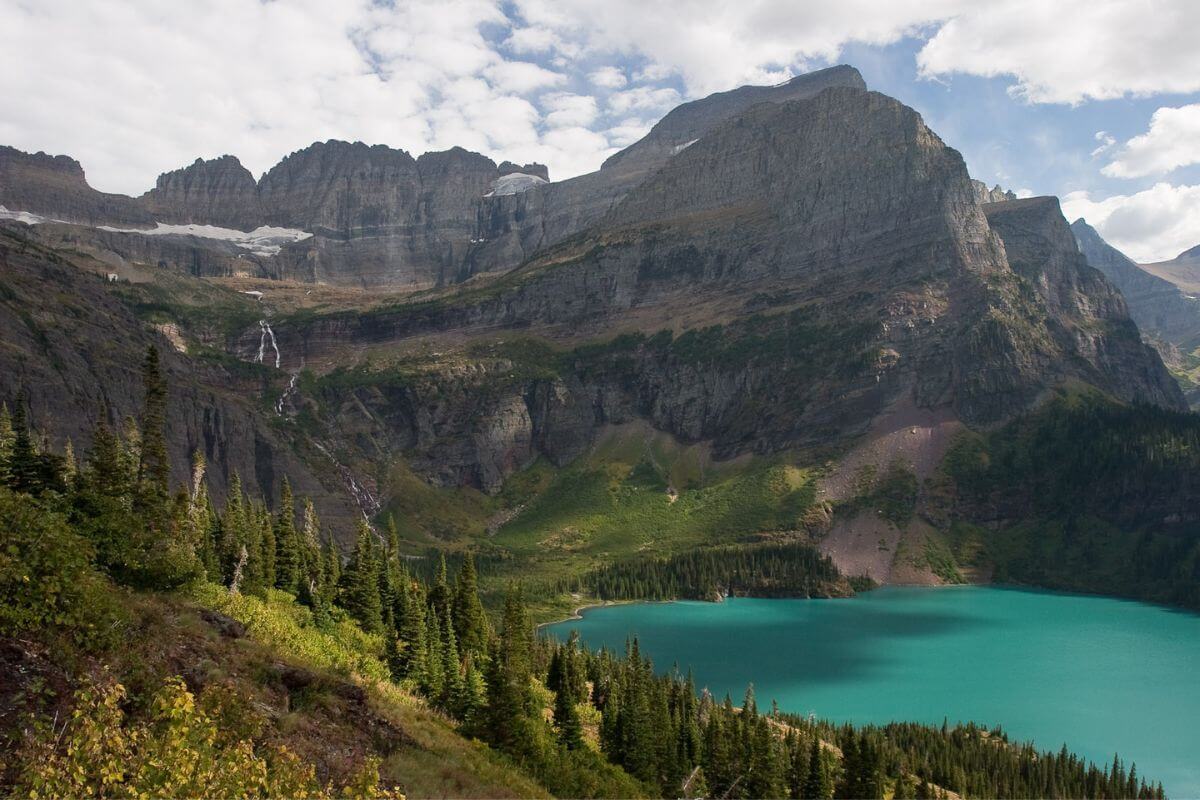 The bright turquoise Grinnell Lake sits in a valley among mountains with trees. 