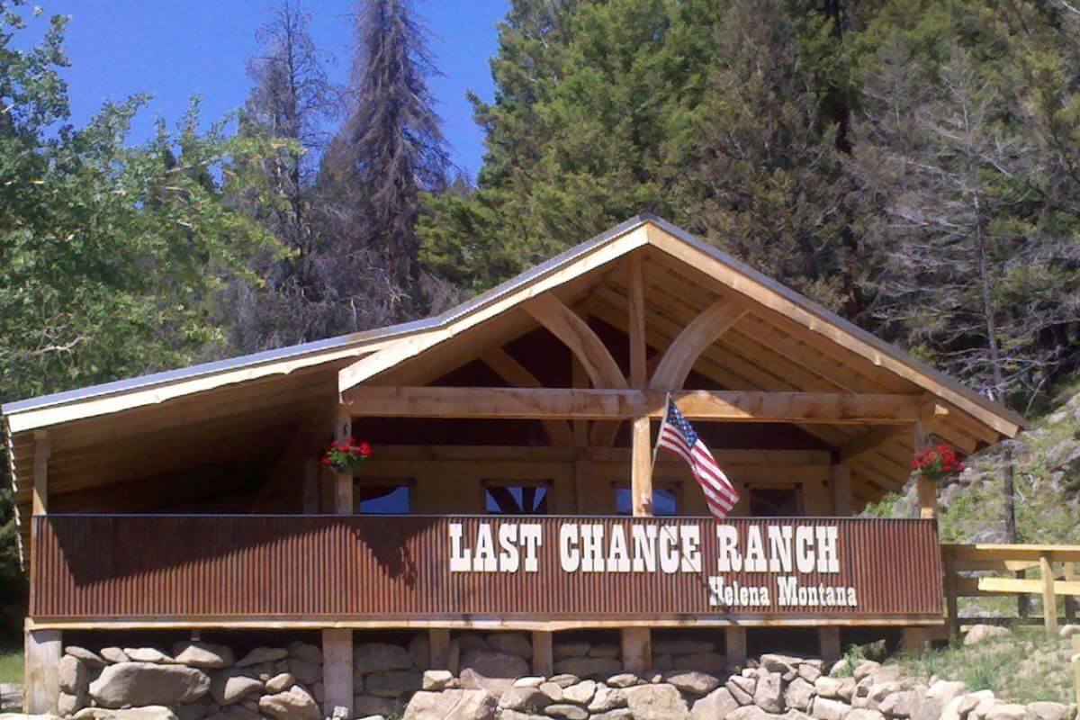 A cabin with a sign reading "Last Chance Ranch" in Helena, Montana. An American flag is displayed, and trees are in the background