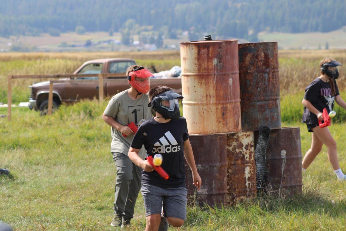 A group of paintball players come out from behind rusty barrels to engage their enemy as seen in the Montana Action Paintball Field.