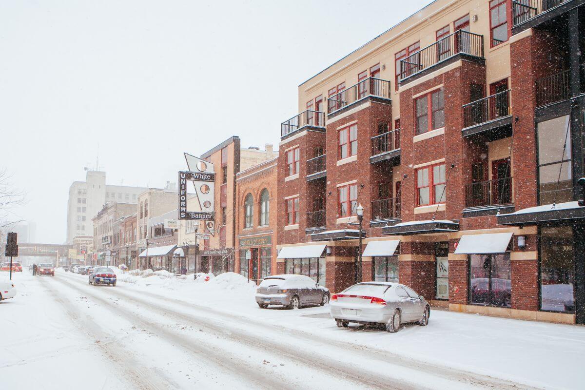 A snowy street with parked cars and buildings in North Dakota, one of the coldest states in the U.S.