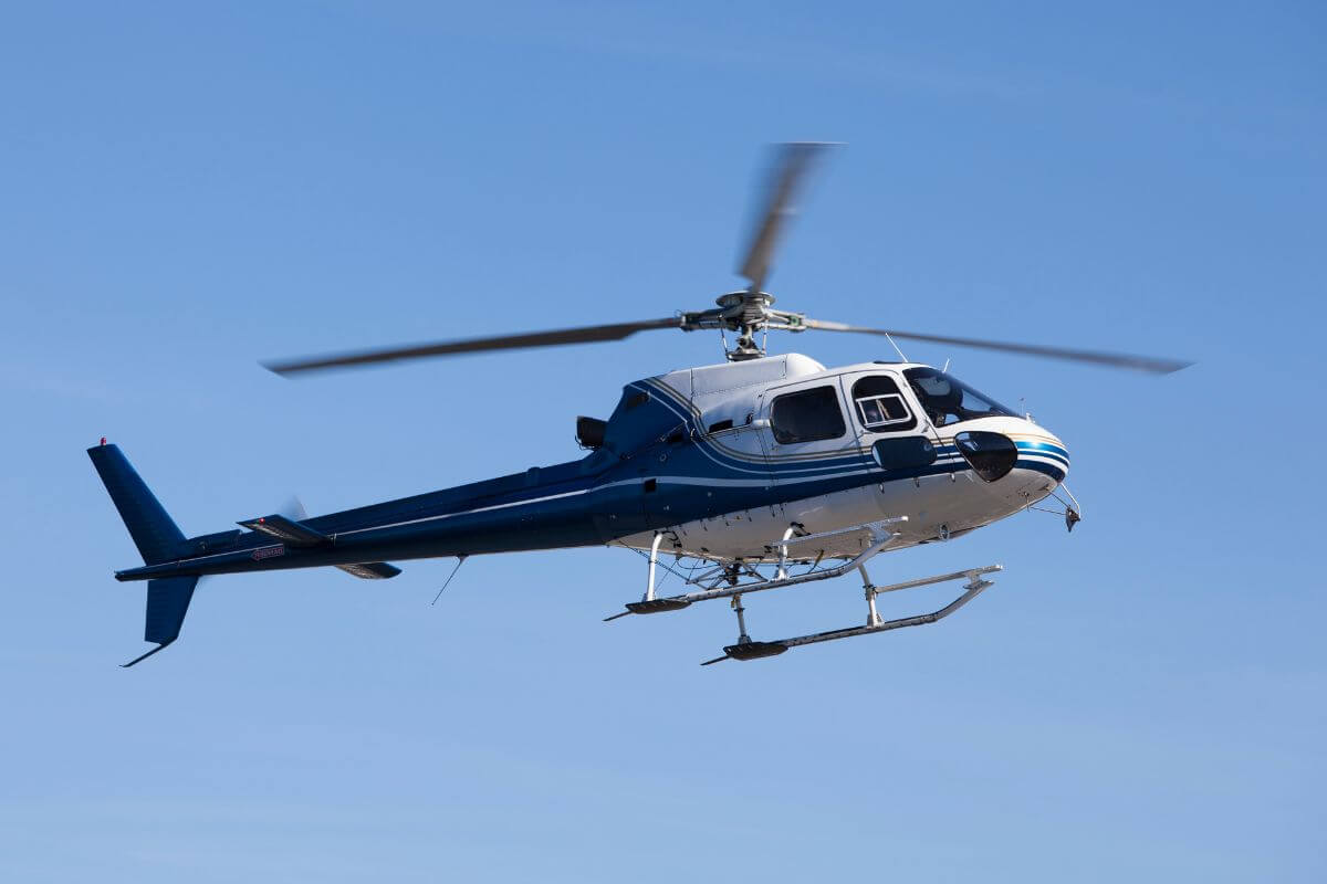 A helicopter in mid-flight against a clear blue sky during one of Triple Creek Ranch's Montana helicopter tours.