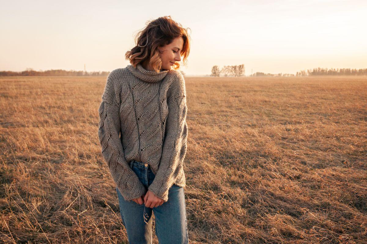 A woman in a sweater standing in a field at sunset in Montana.
