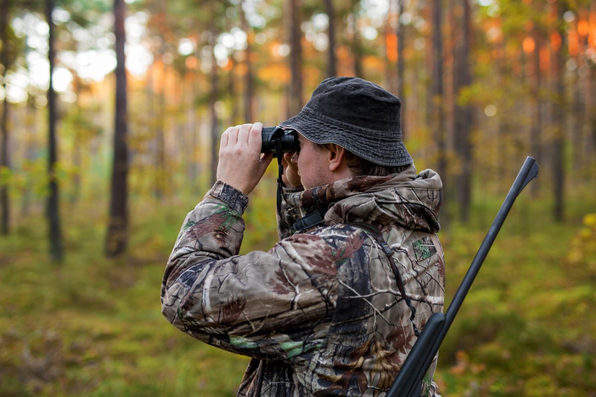 A hunter in Montana, dressed in hunting gear, scans the area through his binoculars for potential antelope prey.