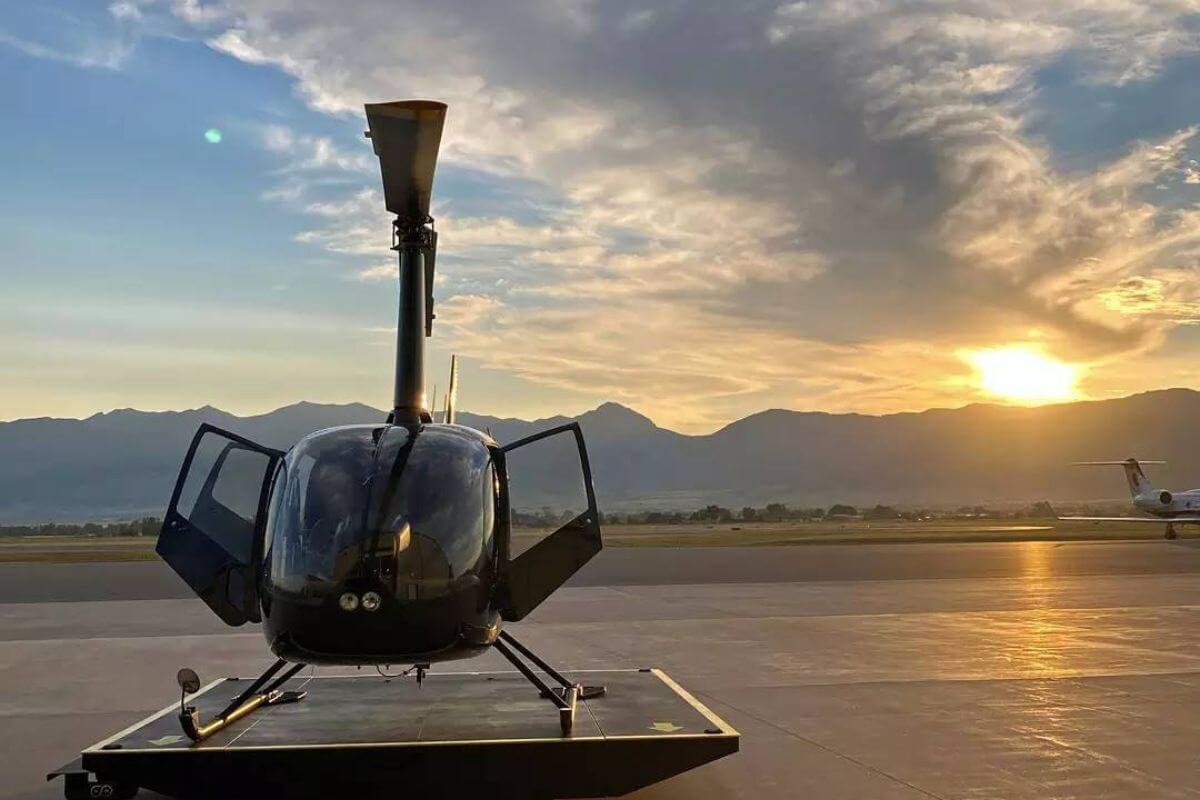 A helicopter sits on an airport tarmac at Central Copters, with mountains silhouetted in the backdrop, ready for Montana helicopter tours.






