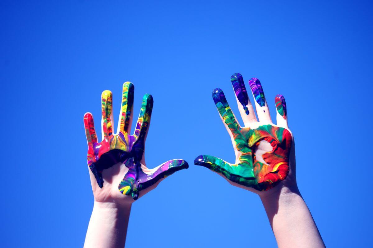 A person's hands painted with different colors against a blue sky 