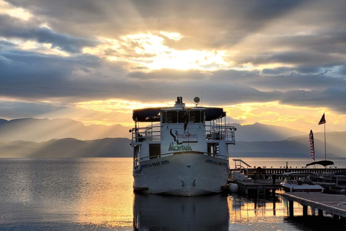 A sunset casts golden hues over a lake with the moored ferryboat called Far West, ready for a Flathead Lake boat tour.