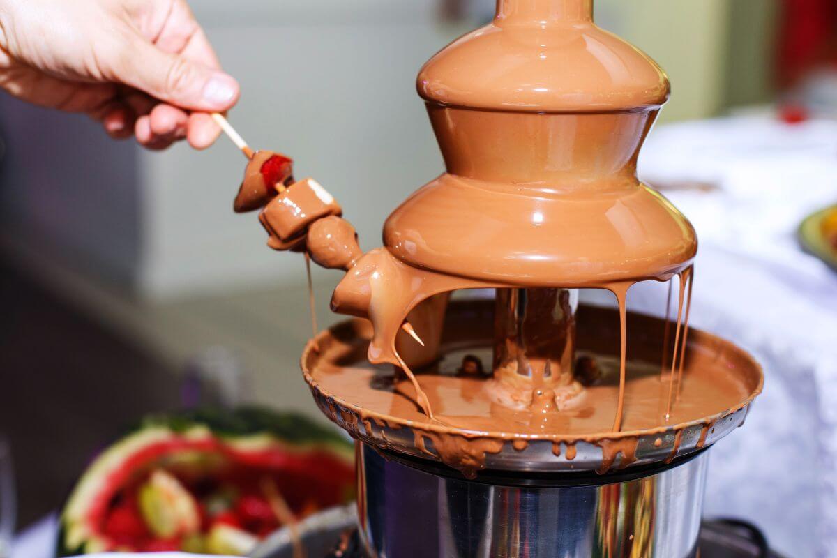 A person dips skewered strawberries into a flowing chocolate fountain at a Montana chocolate tour.