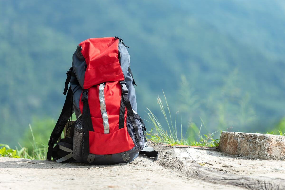 A red and black backpack sits on a path near Ousel Falls, against the backdrop of a lush green mountain landscape 
