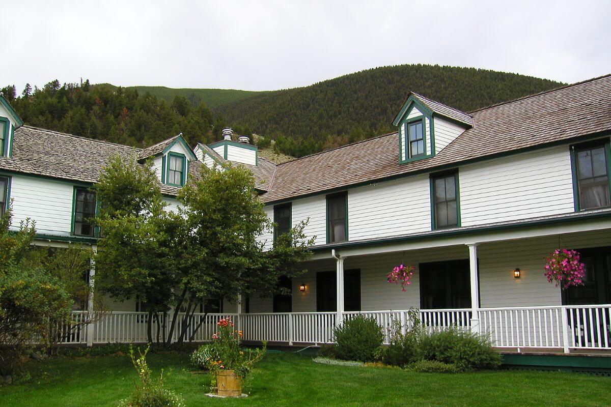 A white and green house with a rust-colored roof looks beautiful amid Montana's lush green surroundings and mountainous background.