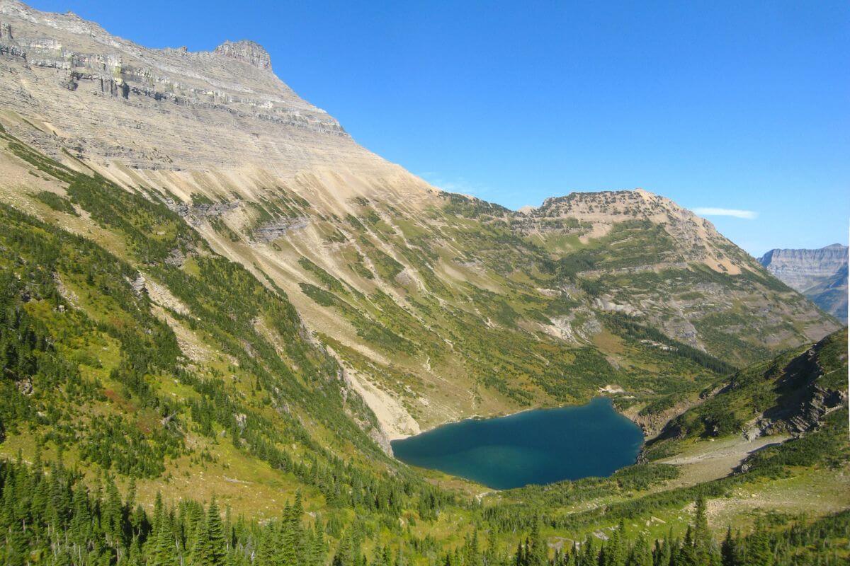 A peaceful mountain scene shows Stoney Indian Lake in a green valley, surrounded by steep, rocky slopes in Montana. 