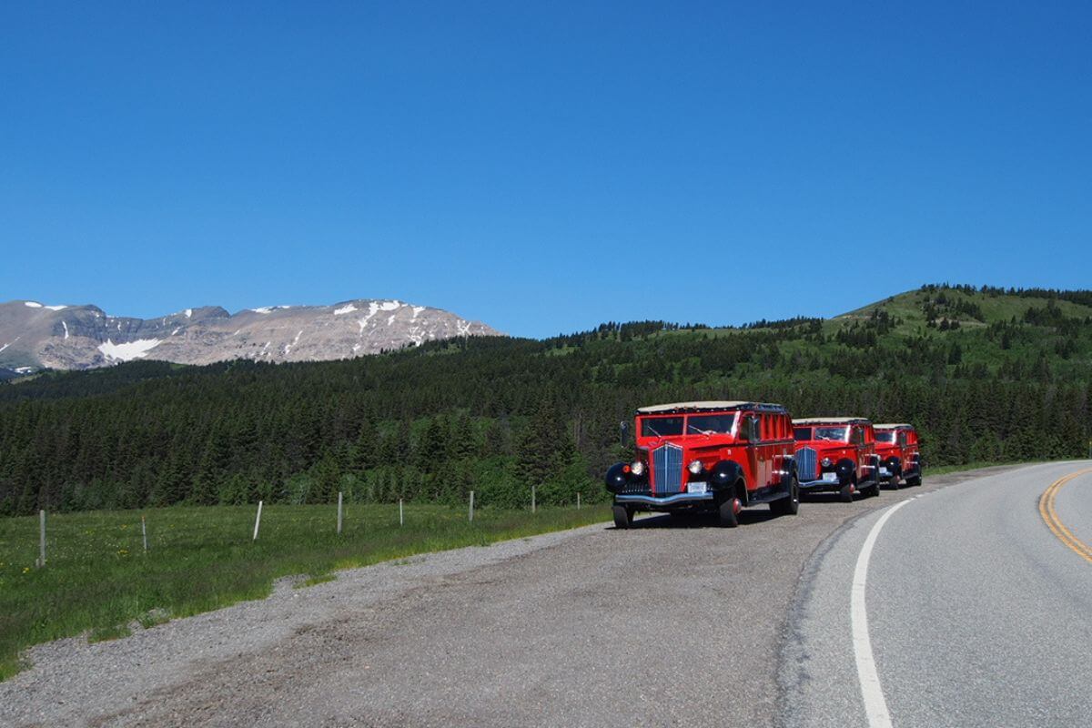 A convoy of red trucks maneuvering along a scenic road with majestic mountains in the background.