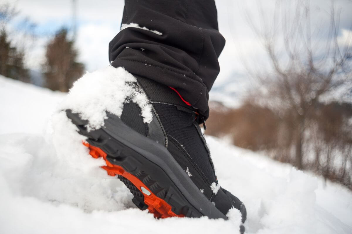 A person's foot, wearing winter boots, is on tiptoe in the snow.