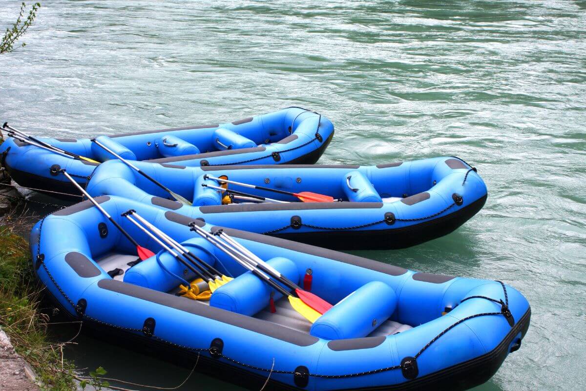 Three blue inflatable rafts with paddles are tied up on the bank of a fast-flowing blue river near Lange Waterfall in Montana.