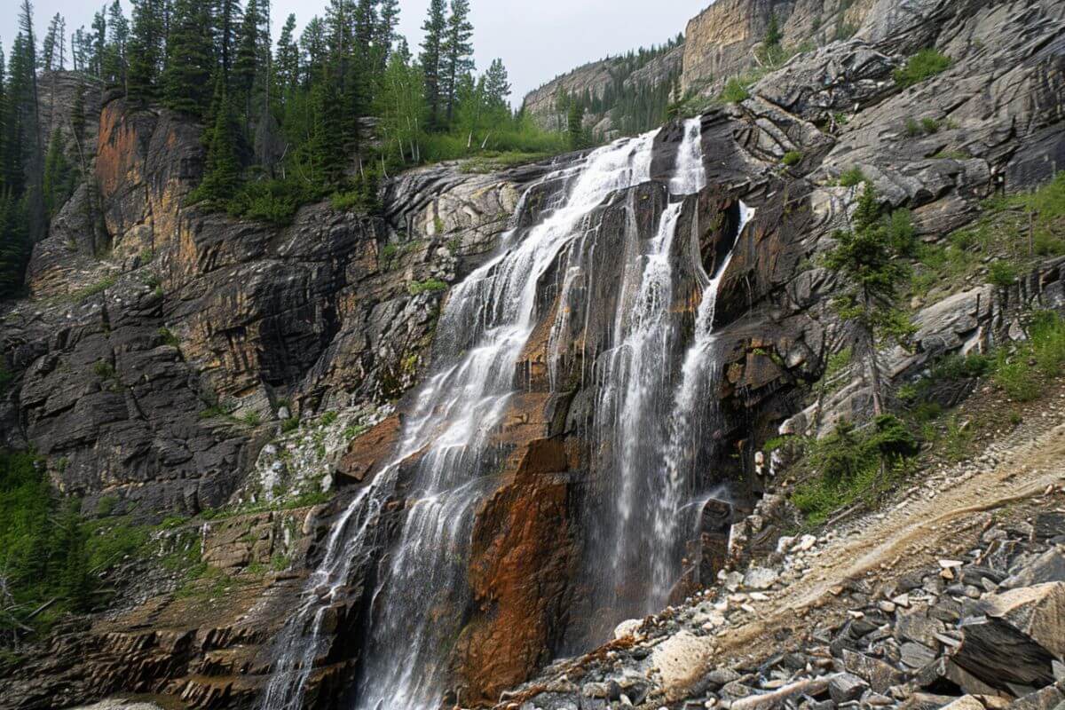 The majestic Impasse Falls cascades down rugged rock faces, surrounded by lush verdant slopes.