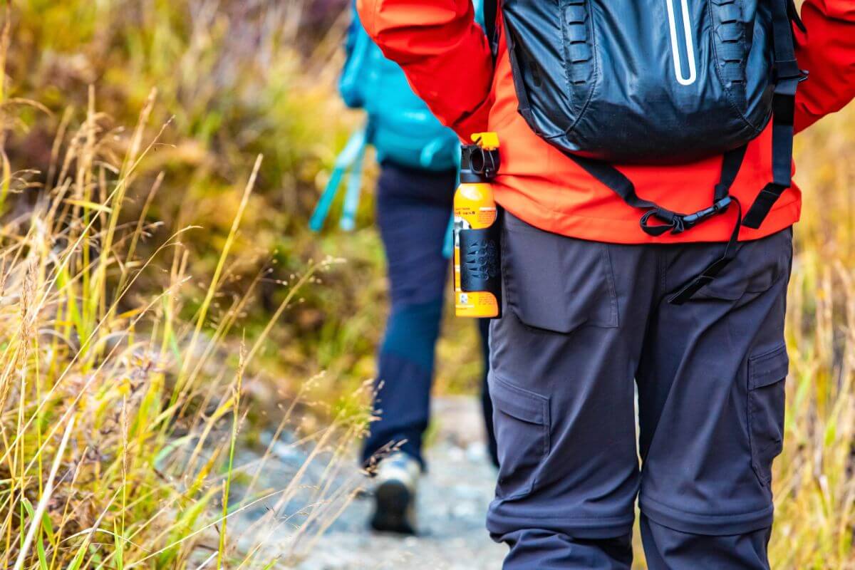 Two hikers with backpacks trekking on a nature trail in Montana, with bear spray attached to one's backpack.