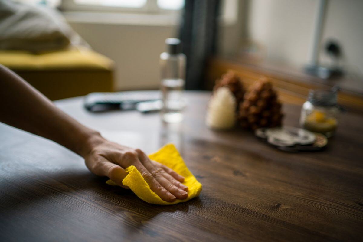 A person gently wiping a yellow cloth on a wooden table in Montana.