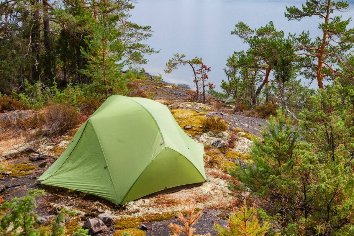 A green tent pitched on a rocky forested coast near the Miche Wabun Waterfall