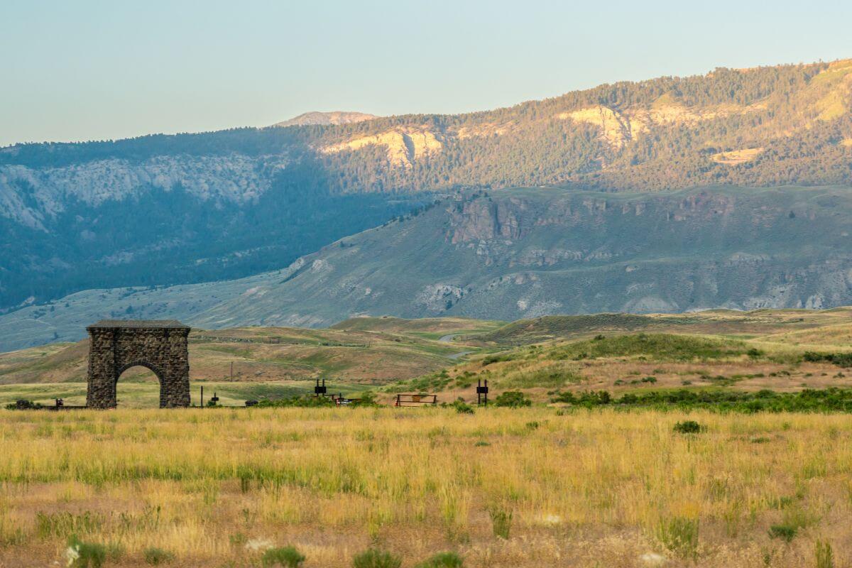 A stone arch nestled in a grassy field in Montana, with a mountain range in the background.