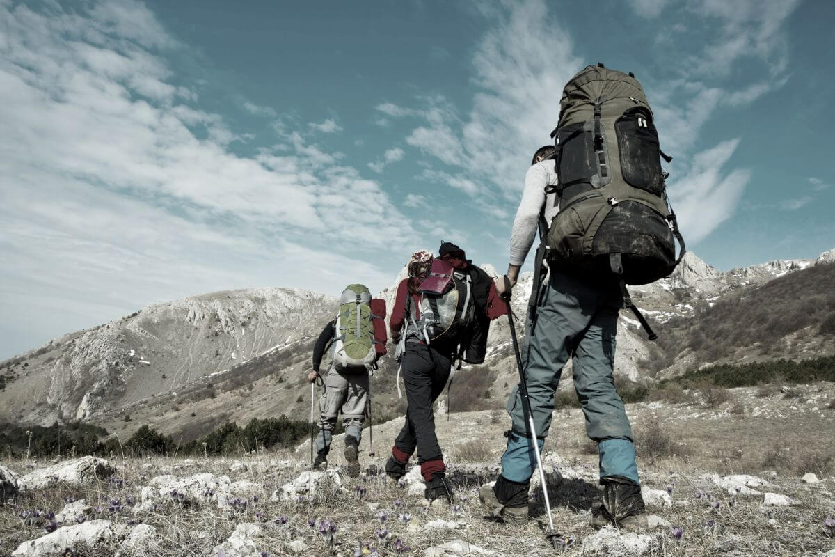 Three hikers with backpacks trekking near Memorial waterfall in Montana.
