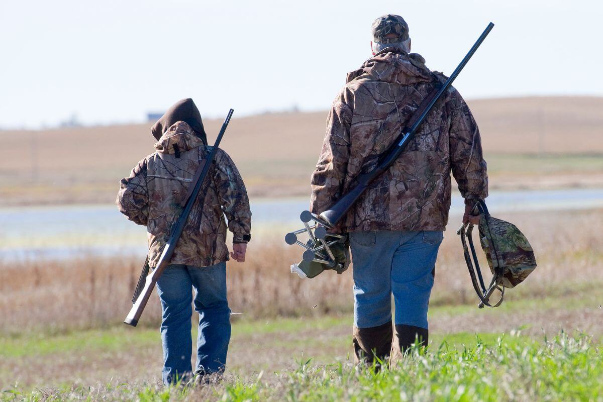 Two duck hunters with rifles walk through a field during a Montana duck hunting trip.