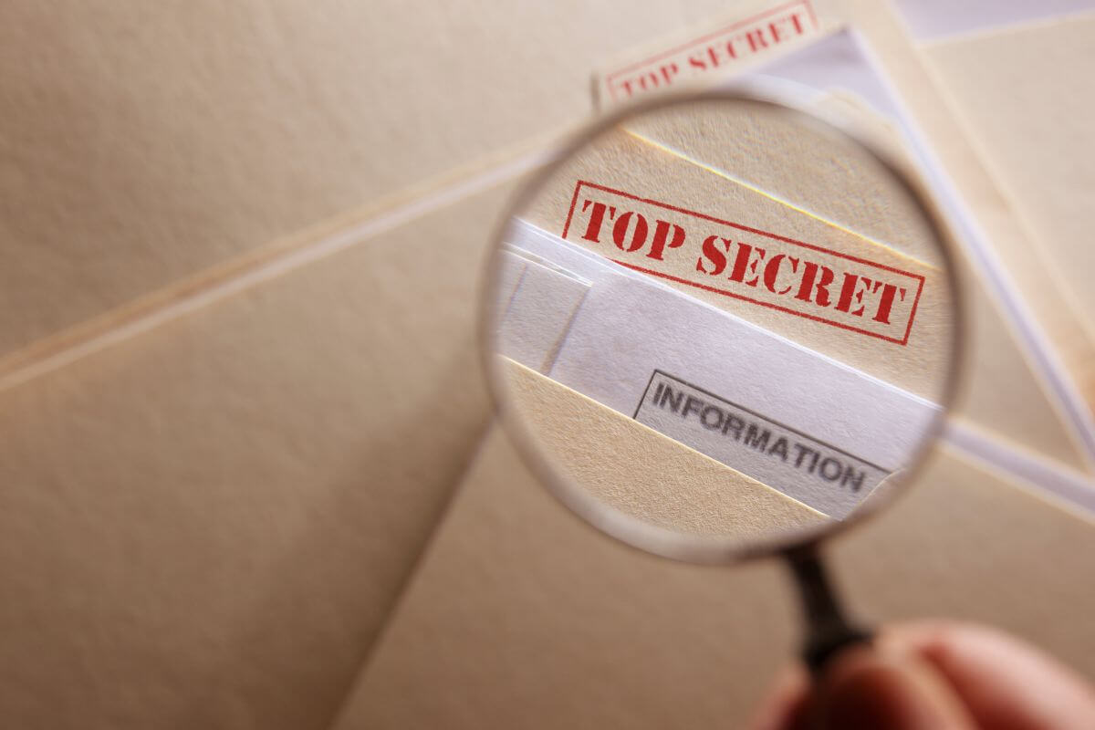 A person is using a magnifying glass to examine top secret documents.