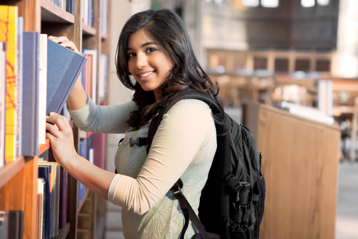 Girl Student Smiling as She Gets a Book in the Library