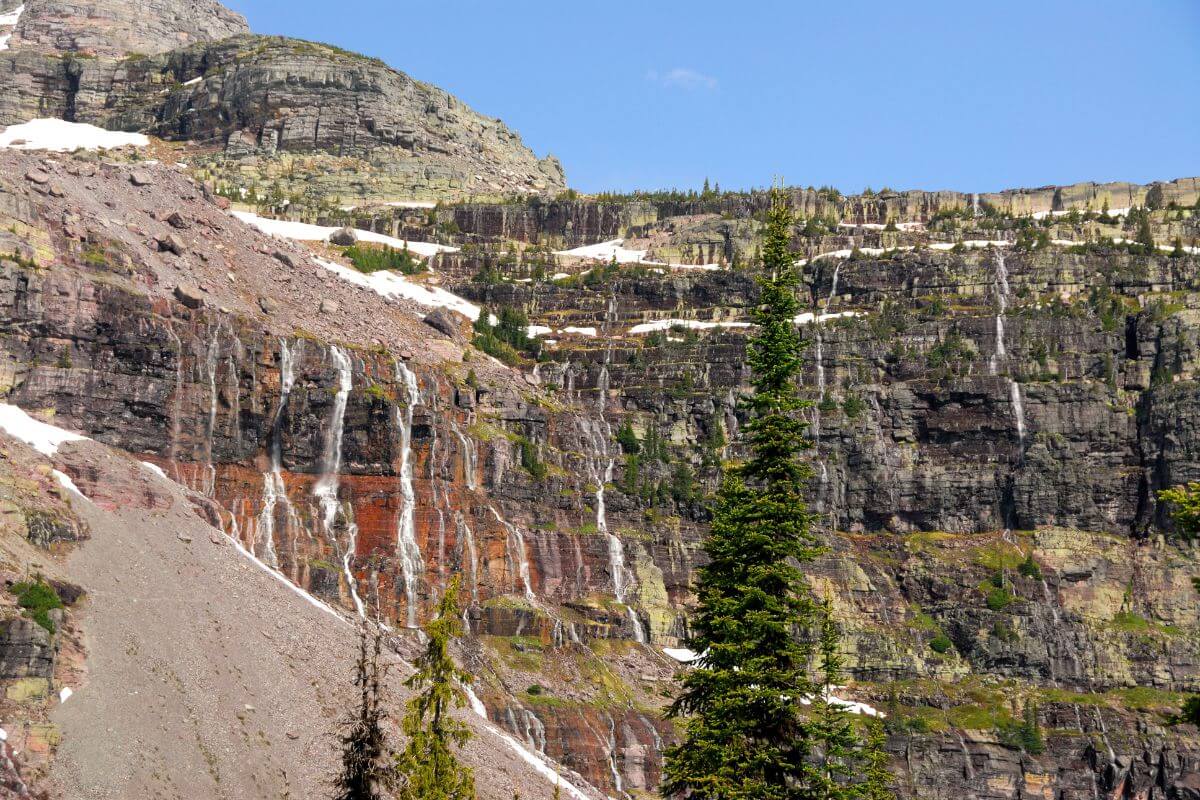 A rugged mountain landscape with multiple thin waterfalls cascading down rocky cliffs also known as Siksika Falls.