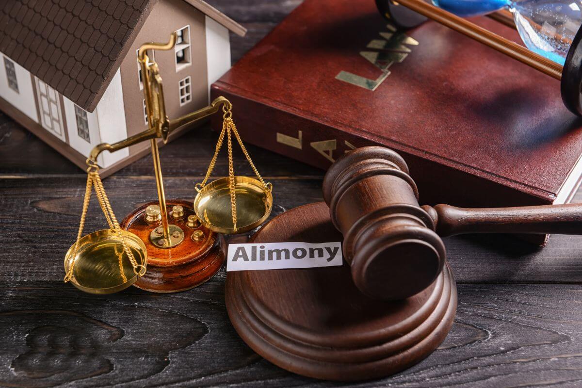 A Miniature Balance Scale, Law Book, Miniature House Model, a Gavel and Sounding Block, and a Small Piece of Paper with "Alimony" Written on It